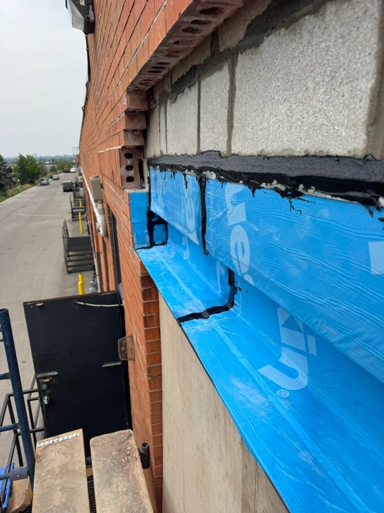 Blue waterproofing membrane installation behind brick facade